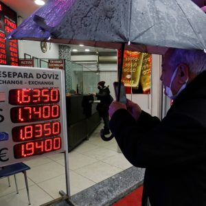 Mann mit Schirm vor Schild mit aktuellen Wechselkursen