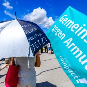 G7-Proteste mit Regenschirm und Armutsbanner