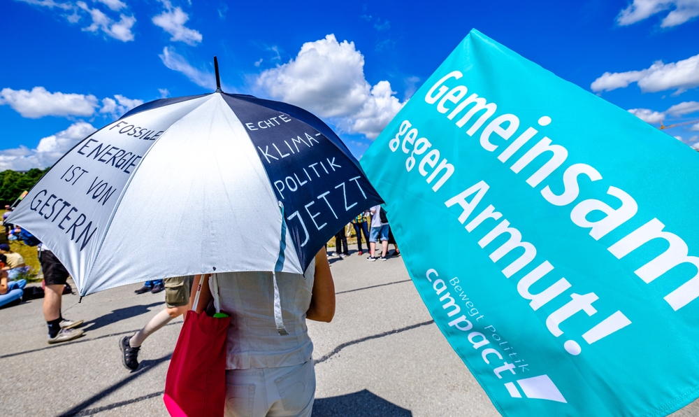 G7-Proteste mit Regenschirm und Armutsbanner