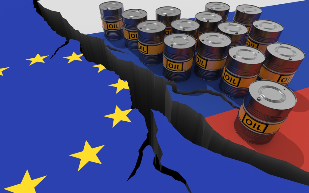 Riss zwischen europäischer und russischer Flagge, Ölfässer auf russischer Seite