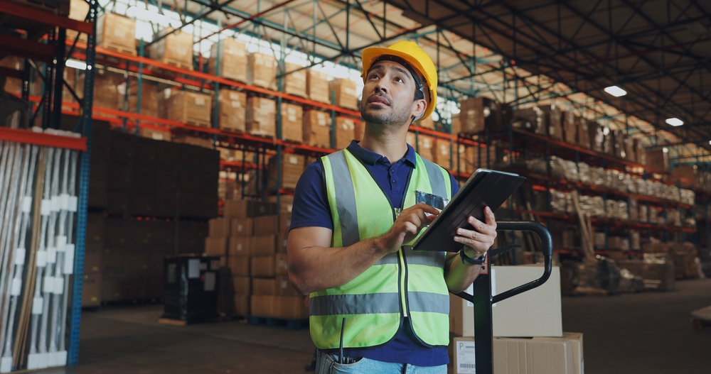 Arbeiter mit Helm und Tablet im Lager